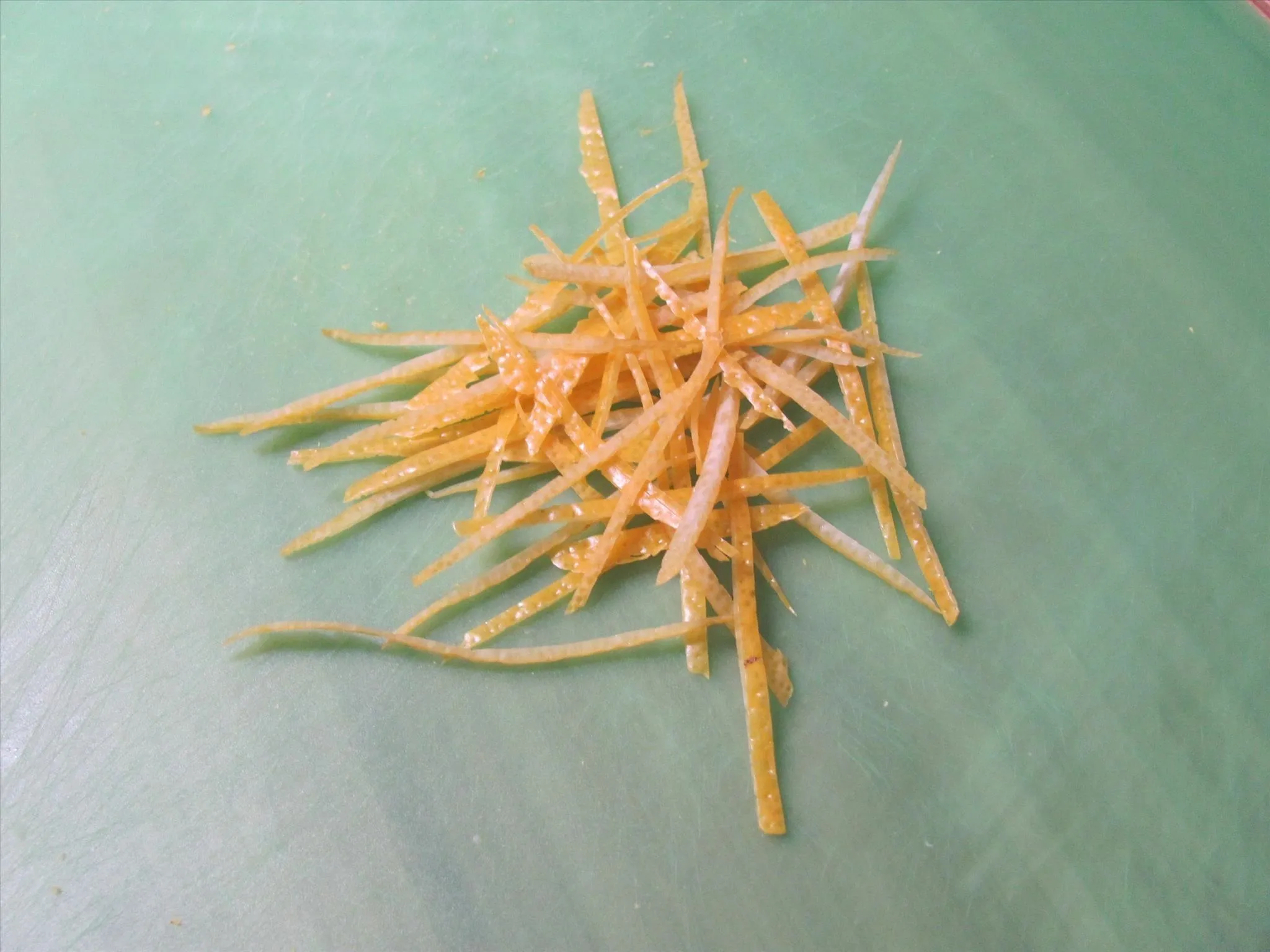 Thin julienne strips of lemon peel stacked on a green cutting board for garnish or recipe prep.